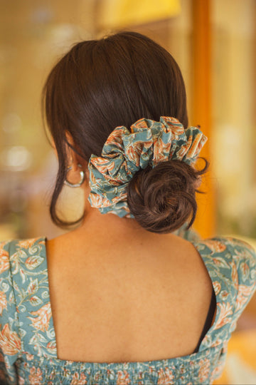 Woman wearing a floral top with a scrunchie in her hair, blurred background