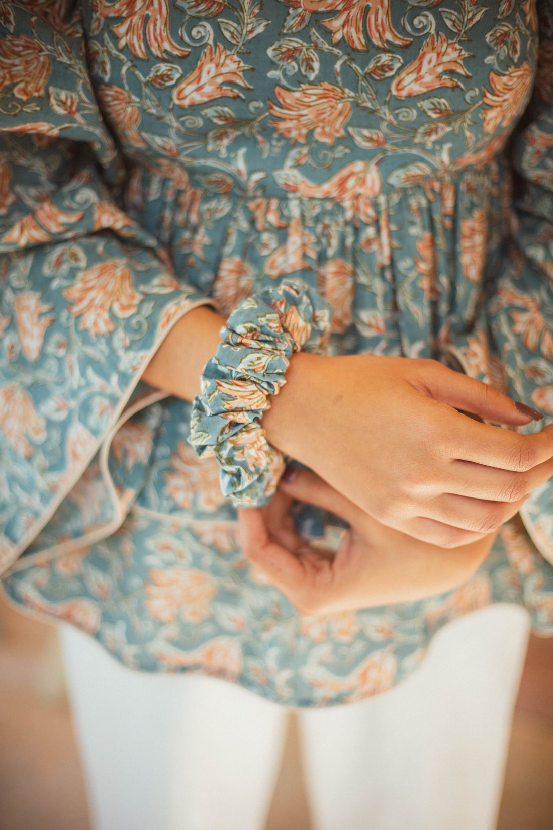 Woman wearing a floral top with a scrunchie in her hair, blurred background