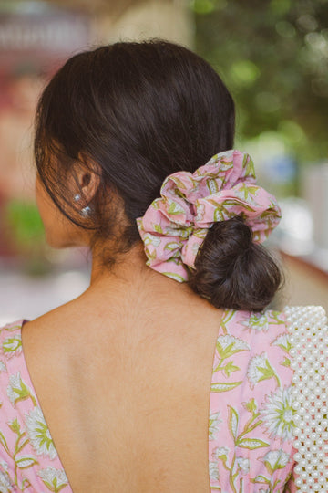 Woman wearing a pink floral dress with a scrunchie in her hair, standing outdoors.