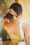 Woman with a floral scrunchie in her hair, wearing a green patterned top.