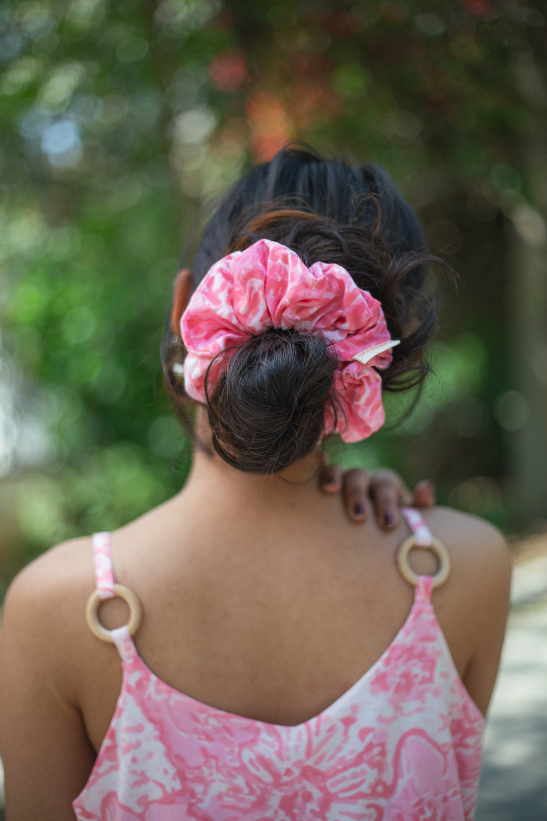 Person wearing a pink scrunchie in their hair with a blurred green background