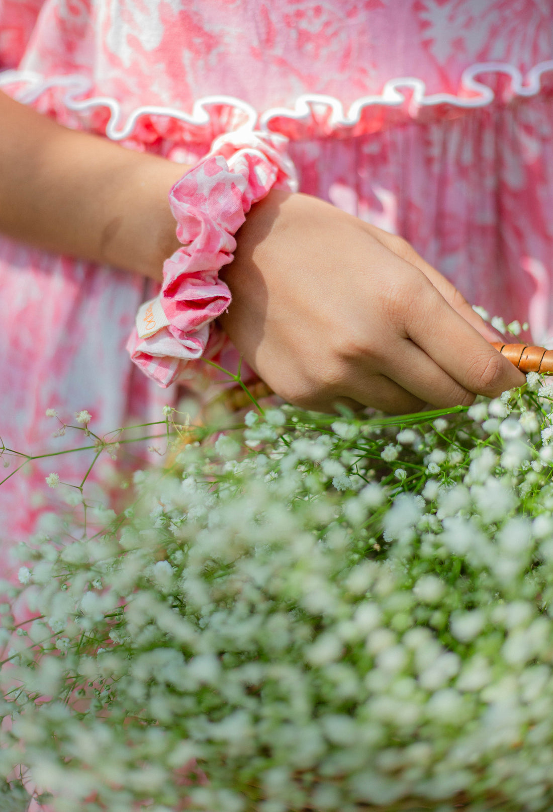 Person wearing a pink scrunchie in their hair with a blurred green background