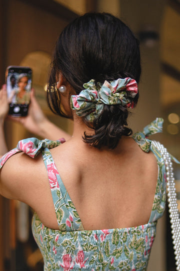 Woman in a floral dress with a pearl-handled bag, taking a photo.